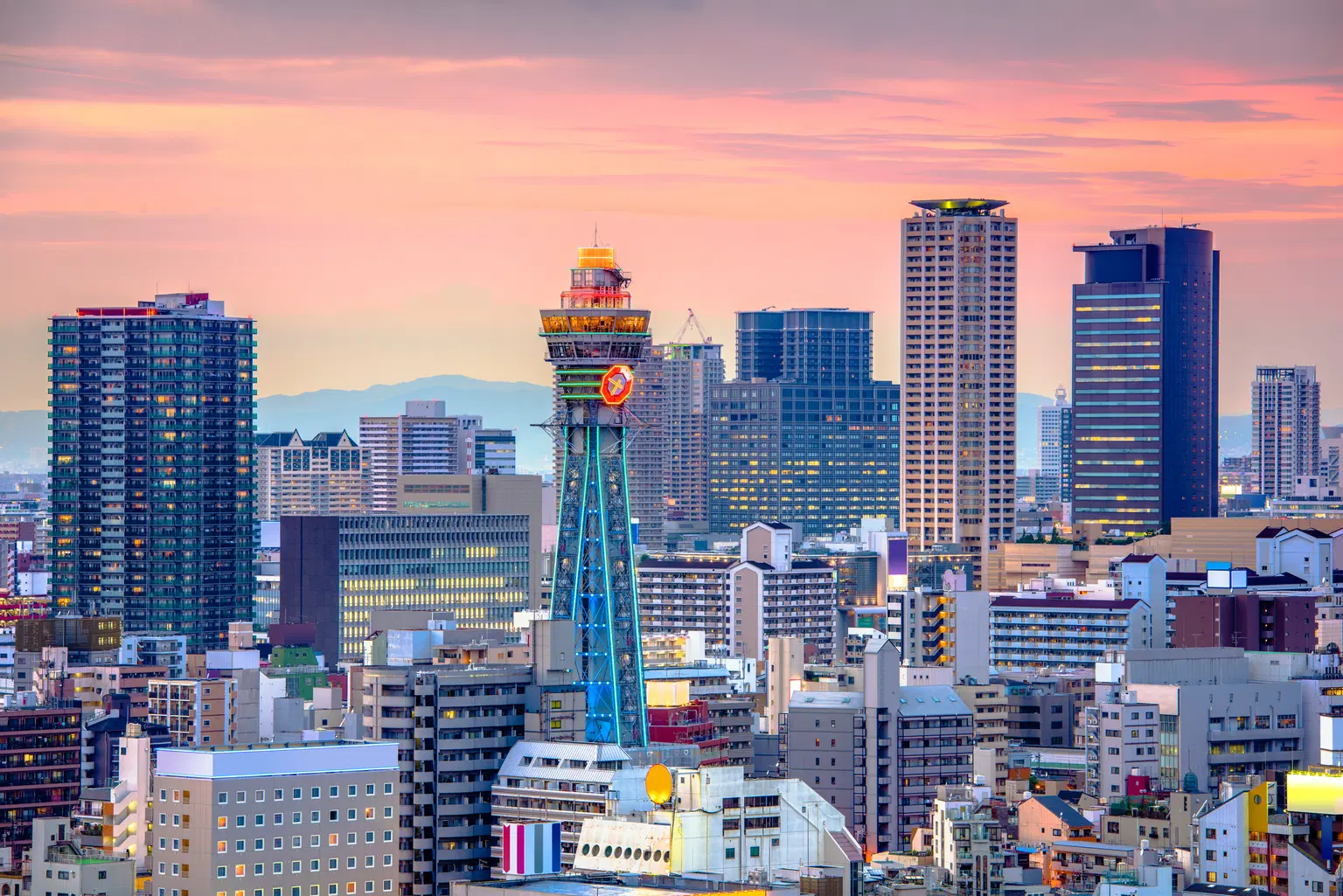 Tsutenkaku Tower in Osaka at sunset, surrounded by city buildings.