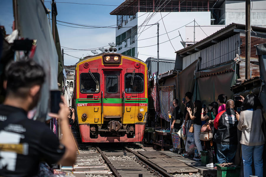 Capture some pictures of a train running across the Maeklong Railway Market