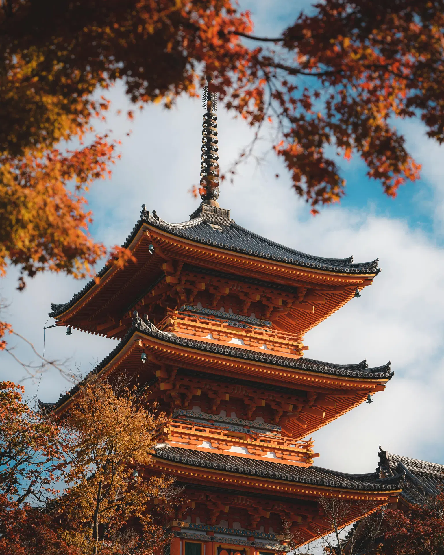 Traditional Japanese pagoda framed by autumn foliage against a blue sky.